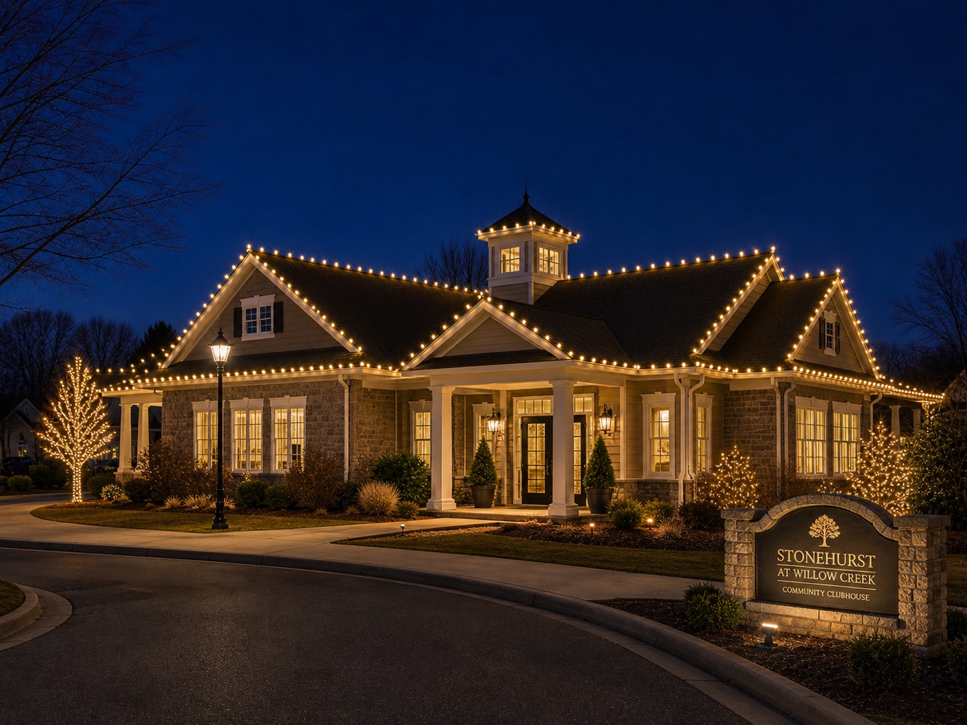 Stonehurst community clubhouse with warm holiday roofline, tree, and monument lighting