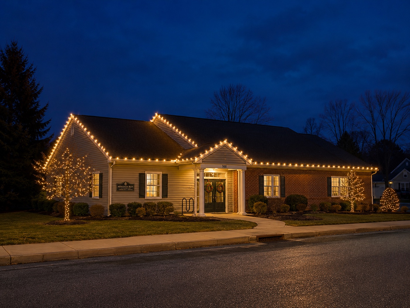 Wingate Run community clubhouse with warm roofline, tree, and walkway holiday lights